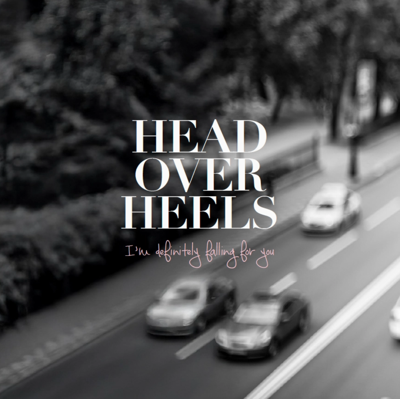 Blurred road with cars and text overlay 'HEAD OVER HEELS I'm definitely falling for you' in a black and white setting.